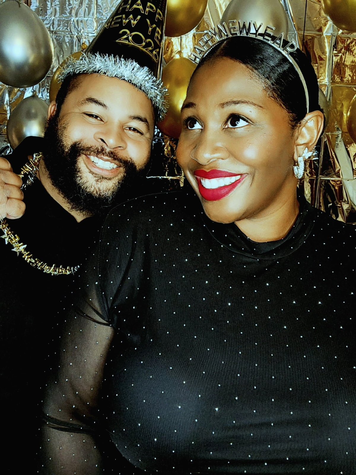 Two people smiling at a New Years celebration with party hats and gold balloons in the background